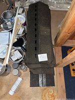 Stack of new roof tiles placed on basement floor near paint cans.