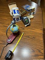 Photo showing the electronic magnetic spinning globe with UPS branded wooden base, the boxed KC Royals mug with a white and blue design, four gold-tone curtain tie backs, Jets paperweight, sport-themed desk clock, and golf motif business card holder arranged on a wooden table with measuring tape for scale.