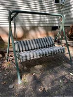 Outdoor swing with green metal frame and striped cushioned seat viewed from the front