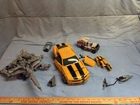 Overview photo showing all four primary Transformers toys and detached parts on blue background with measuring ruler for scale.