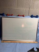 White dry erase board with silver metal frame, stained, shown with ruler for scale and dumbbells in background (excluded).
