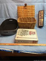 Black woven basket, brown wicker basket with lid and leather strap, and boxed J.K. Adams Co. 12-bottle wine rack displayed on a blue cloth backdrop with a measuring ruler.