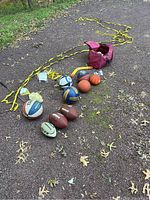 Outdoor photo of various youth-sized sports balls arranged on the ground with a red carrying bag and long yellow ropes from a sport net.