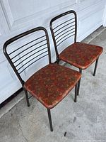 Two metal-legged folding chairs with colorful vinyl cushioned seats against a garage door, side angle.
