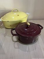 Yellow oval and maroon round enameled cast iron Dutch ovens together