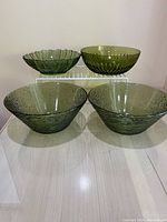 Four green glass bowls displayed, two on top shelf and two larger on table, showing size and design variety