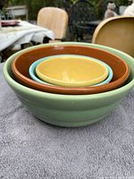 Side view of 4 nested Bauer California Pottery bowls in green, orange, blue, and yellow glaze showing their stacked configuration.
