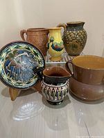 Group of six glazed ceramics displayed on a shelf, showing variety of shapes, colors, and patterns