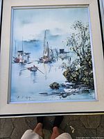 Full view of the framed painting showing boats, water, and trees under soft lighting.