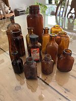Front angle showing full set of 14 assorted brown glass bottles with varying sizes and shapes including one with a black screw cap and label