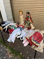 Photo showing a group of vintage dolls including two large Dutch walking dolls with colorful costumes and several other assorted vintage dolls lying on a bench.
