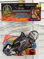 Photo of the packed 15-piece Halloween decorating kit showing a large skeleton window cling and other colorful decorative items inside the package with a 'Haunted Hacks' branding.