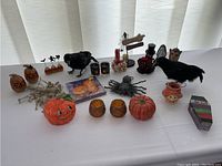 Photo showing Halloween decorative items including pumpkins, ravens, spider, candles, and napkins arranged on table