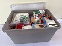 Wide view of gray plastic bin with lid open showing original boxes and loose village accessories inside.