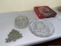 Glass platter, covered dish, metal Christmas tree trivet, and boxed fruit bowl on table