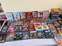 View of approximately 35 DVDs arranged in grid on table including Pokémon, animated Disney titles, Barbie movies, and live action films.