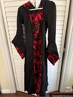 Front view of the black dress showing the red patterned central panel and hood.