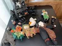 Photo showing the entire collection of Halloween decorations on a black surface, including the haunted mansion, stuffed figures, and plastic animals.