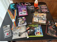 Full overview of various unopened and lightly used Halloween makeup and costume accessories including jewelry, suspenders, makeup, and fake blood gel on table.