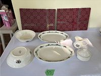 Full set showing the two serving plates, two serving bowls, creamer, sugar bowl, and placemats on a table.