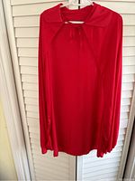 Front view of red knee-length cape with hood and tie neck detail, hanging on a hanger.