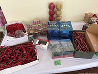 Wide top-down view of the boxed and loose Christmas decorations including decorative bulbs, string lights, and bead garlands packed in cardboard boxes for easy pickup.