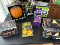 Photo of various Halloween decoration items including an artificial pumpkin, Peepin Peepers LED spotlight, boxed strobe light, Spirit Strobe 360 light, mini flame light, and a small bag of colorful plastic decoration faces.
