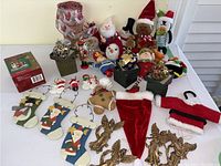 Photo of the assortment of Christmas plush ornaments, wooden stockings, golden angels, decorative balls in boxes, ribbons, and a red sequin stocking hat arranged on a white surface.