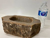 Side profile view of the rough textured carved stone basin with hollow center and a water bottle for scale.