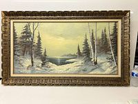 Full front view of the framed oil painting showing winter landscape with snow-covered trees and lake beneath a yellow sky.