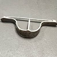 Side view of the curved silver bun holder, showing the 1937 engraving on the front side and the shape of the piece.