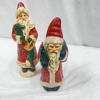 Two vintage Santa Claus figures with crackle finish, red coats, white trim, and tall red hats, posed side by side.