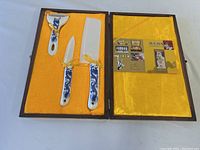 Full view of the Asian luxury porcelain cutlery set in a yellow fabric-lined box, including knife, cleaver, and peeler with blue dragon decoration