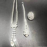 Full view of two rhinestone crystal necklaces and one floral brooch on black background