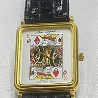 Front view of rectangular gold-tone bezel watch with King of Diamonds playing card face decorated with rhinestones, black textured strap.