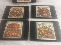 Four of the five Pimpernel plate mats laid out, each with a black border and a central colorful fruit basket print.