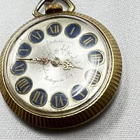 Close-up of watch face with visible brand name Endura, Roman numerals in blue and gold, floral engraving, and gold decorative hands.
