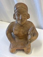 Front angled view of the vintage stoneware sculpture of a seated woman holding a baby figure. Shows facial features, earrings, and detailed hand positions.