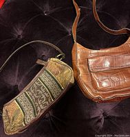 Two vintage Fossil handbags displayed on dark velvet fabric, showing a tan faux crocodile leather bag with flap and a smaller fabric logo patterned bag.