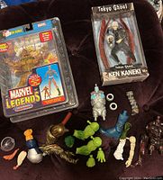 View of boxed Sabretooth figure, loose Marvel Legends Giant Man build-a-figure parts, and boxed Tokyo Ghoul Ken Kaneki figure on dark surface.