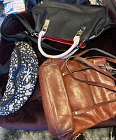 Lot of three bags arranged on surface: black and white patterned fanny pack with zipper and Reebok logo, brown leather purse, and large black handbag with white handles