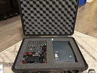 Open case showing Brother P-touch 2500pc labelling machine on right side and multiple tape cartridges with power cables on left.