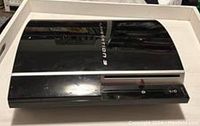 Top and front angled view of the black Fat Model PlayStation 3 console showing the PlayStation 3 logo and disc drive.