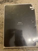 Front view of the iPad Smart Cover packaging, showing the product name and grey cover inside a plastic wrapping.