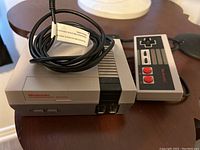 Mini Nintendo NES Classic Edition console showing front power and reset buttons with Nintendo Entertainment System branding, connected to controller cable.