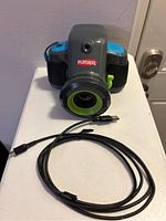 Front view of the Playskool children's digital camera showing lens, body, and attached USB cable.