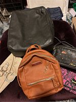 Five bags arranged together showing a variety of purses and backpacks in different colors and styles.