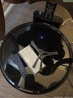 Top view of black glossy Robit robot vacuum cleaner displaying blue illuminated power button with remote control, replacement filter, cleaning brush, and tool resting on top, showing all included accessories.