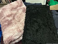 Two small rugs side by side, one light pink and one black, showing their texture and size.