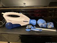 View of Steam Xpress handheld garment steamer and accessories laid out on a piano surface under bright lighting.